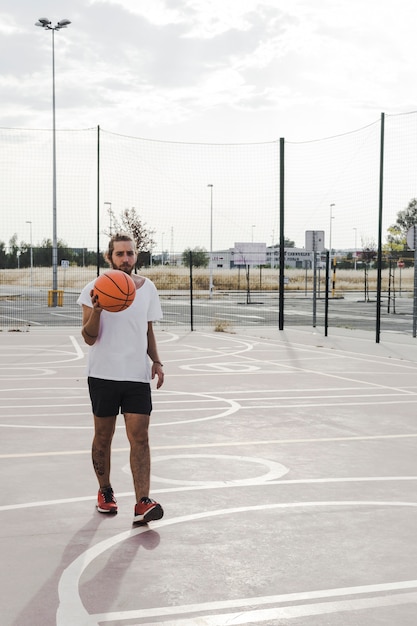 Foto gratuita giovane giocatore maschio con pallacanestro in tribunale