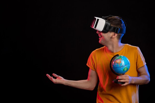 Young male playing virtual reality holding globe on dark surface