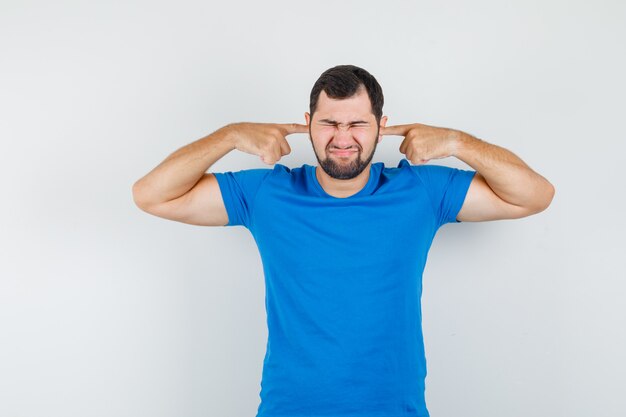 青いTシャツの指で耳を塞いでイライラしている若い男性