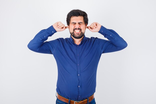 Young male plugging ears with fingers in royal blue shirt and looking enduring. front view.