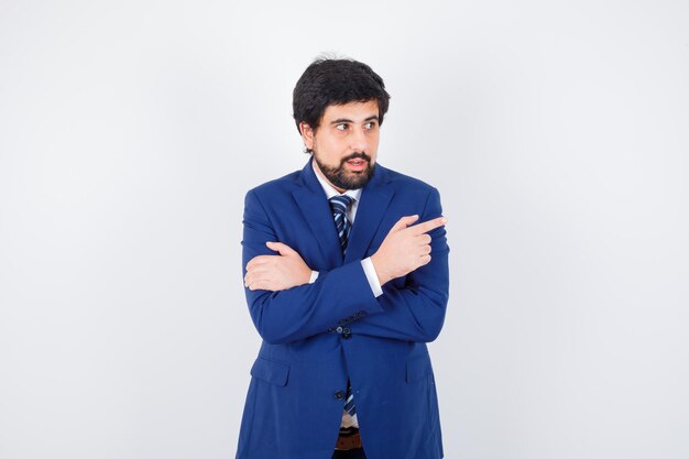 Young male pointing aside in shirt,jacket,tie and looking focused , front view.