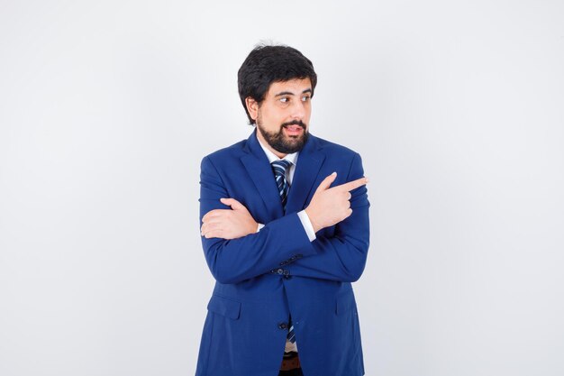 Young male pointing aside in shirt,jacket,tie and looking joyful. front view.