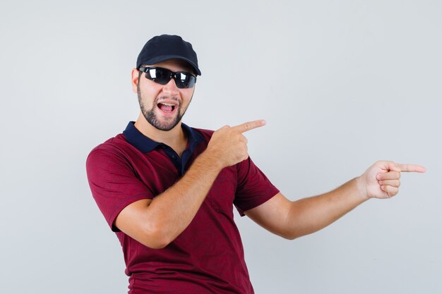 Young male pointing aside in t-shirt,black glasses and looking energetic. front view.