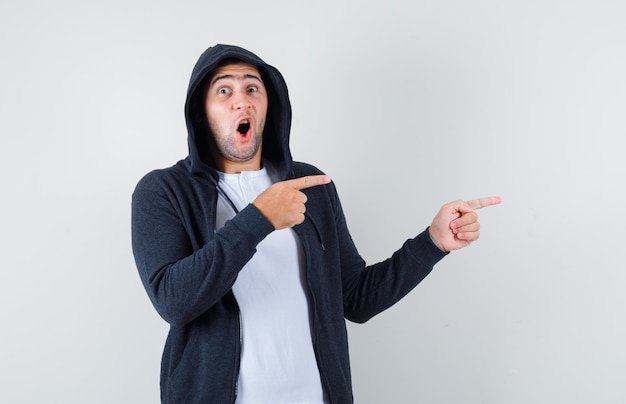 Young male pointing aside in t-shirt, jacket and looking astonished , front view.