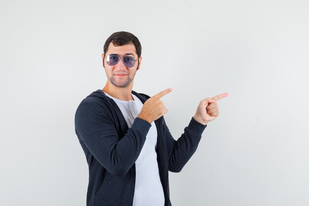 Young male pointing aside in t-shirt, jacket and looking optimistic , front view.