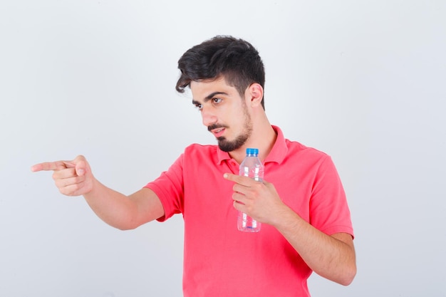 Young male pointing aside in t-shirt and looking focused. front view.