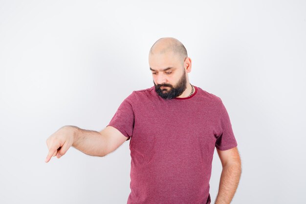 Young male pointing aside in t-shirt and looking focused. front view.