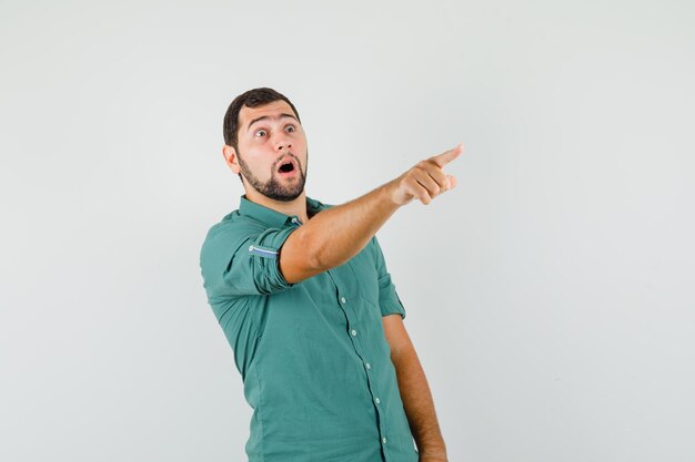 Young male pointing away in green shirt and looking surprised. front view.