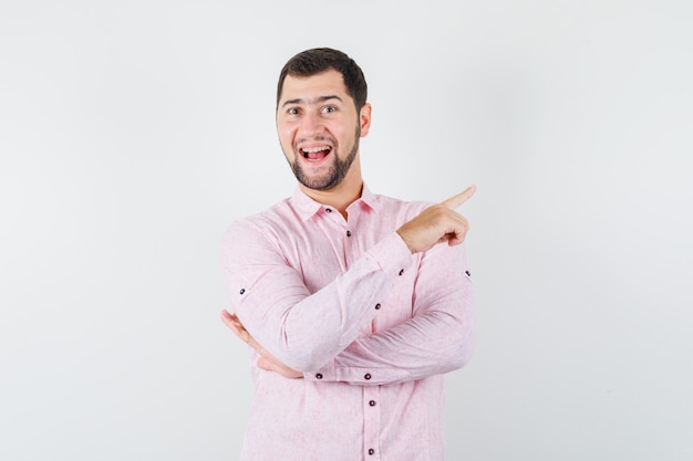 Young male pointing away in pink shirt and looking cheerful