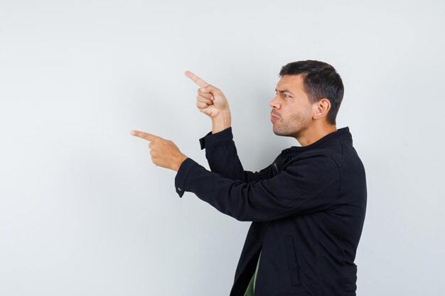 Young male pointing away in t-shirt, jacket and looking focused. .