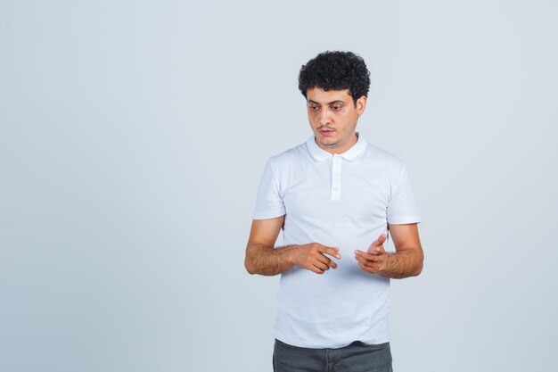 Молодой мужчина указывает в сторону, глядя вниз в белой футболке, штанах и задумчиво, вид спереди.