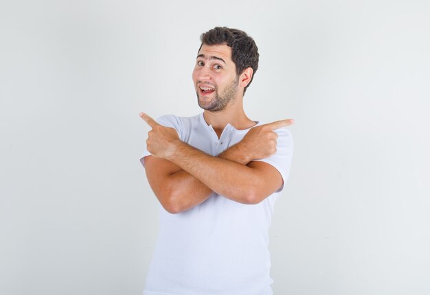 Young male pointing away with crossed arms in white t-shirt and looking happy