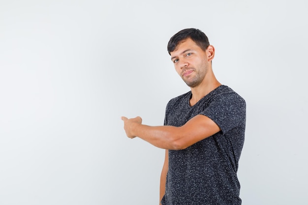 Young male pointing to back in black t-shirt and looking assured. front view. space for text