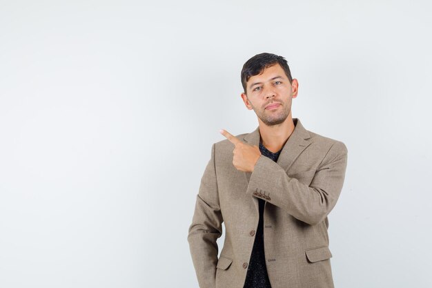 Young male pointing back in grayish brown jacket and looking focused , front view. space for text