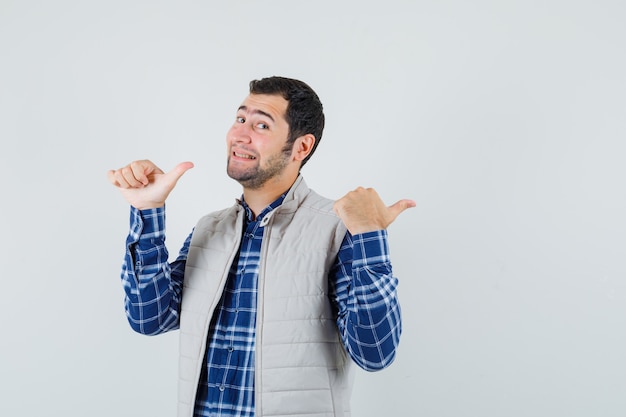 Young male pointing back in shirt,sleeveless jacket , front view.