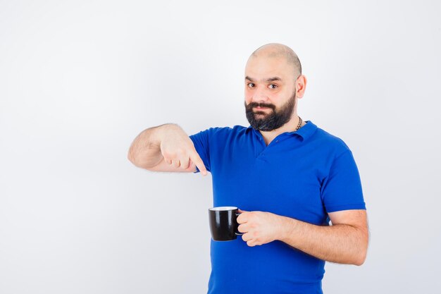 Young male pointing to black cup in blue shirt and looking positive , front view.