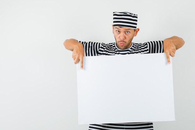 Young male pointing at blank canvas in striped t-shirt hat 