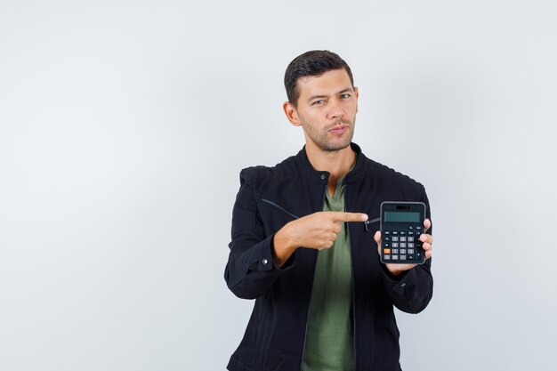 Free photo young male pointing at calculator in t-shirt, jacket and looking sensible , front view.