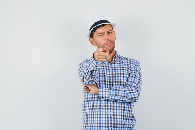 Young male pointing at camera in checked shirt, hat and looking confident