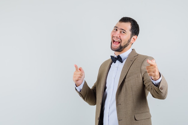 Young male pointing at camera in suit and looking merry , front view.