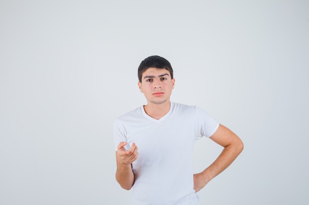 Young male pointing at camera in t-shirt and looking careful , front view.