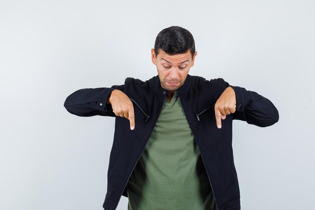 Young male pointing down in t-shirt, jacket and looking focused. front view.