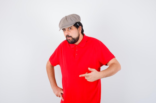 Молодой мужчина указывает вперед в красной футболке, кепке и выглядит уверенно. передний план.
