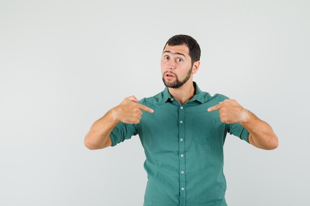 Young male pointing himself in green shirt and looking focused , front view.