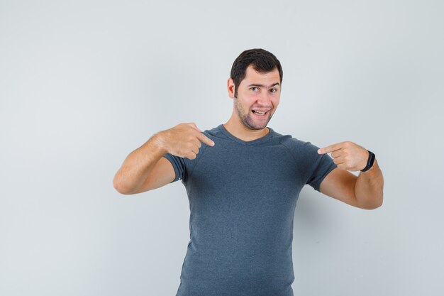 Young male pointing at himself in grey t-shirt and looking proud , front view.