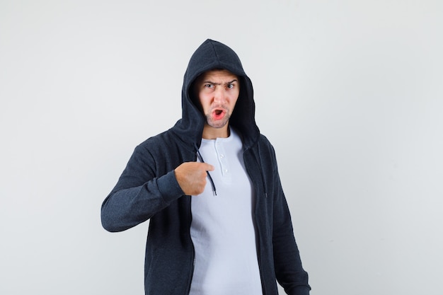 Young male pointing at himself in t-shirt, jacket and looking angry. front view.