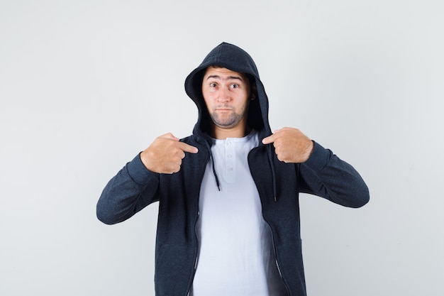 Young male pointing at himself in t-shirt, jacket and looking puzzled , front view.