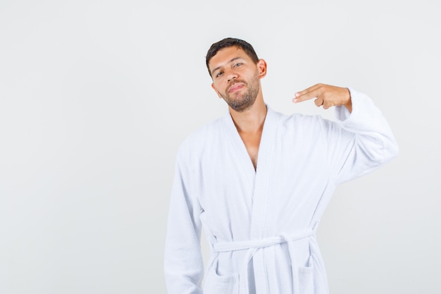 Young male pointing at himself with fingers in white bathrobe and looking confident , front view.