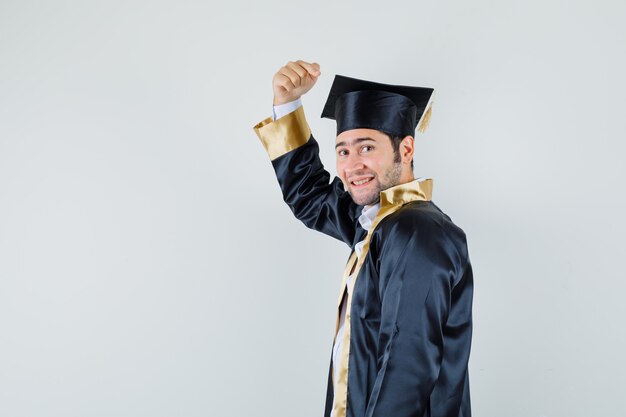 Молодой мужчина указывая на его черную кепку в униформе выпускника и выглядел счастливым. .