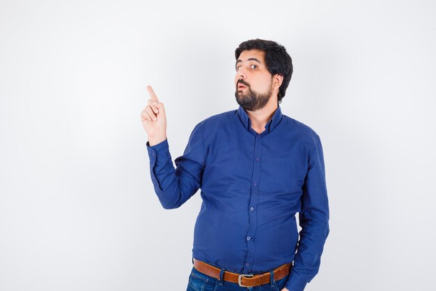 Young male pointing at the left corner in shirt, jeans and looking funny. front view.