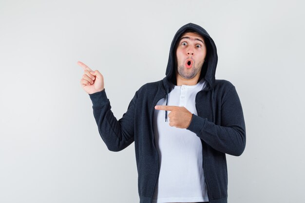 Young male pointing to the left side in t-shirt, jacket and looking surprised. front view.