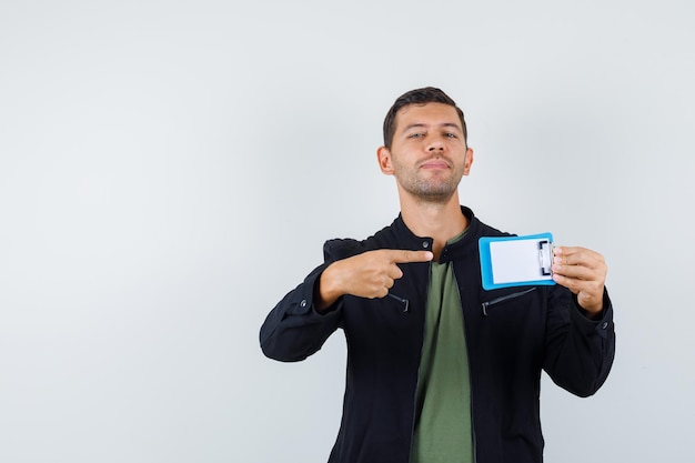 Free photo young male pointing at mini clipboard in t-shirt, jacket and looking cheery. front view.