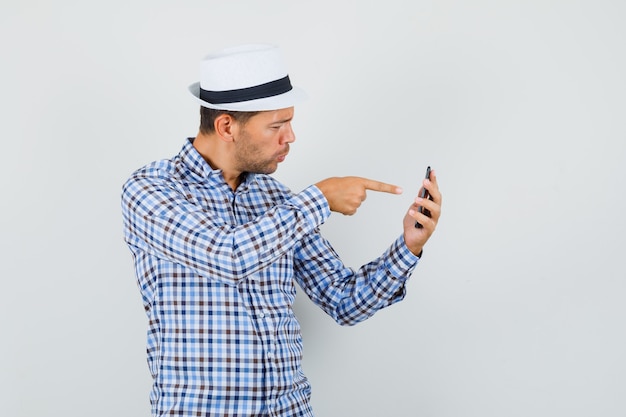 Young male pointing at mobile phone in checked shirt