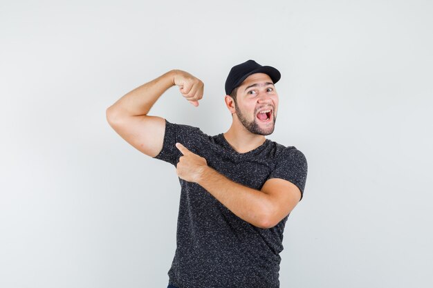 Young male pointing at muscles in t-shirt and cap and looking confident