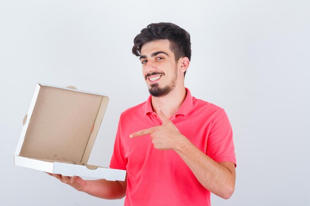 若い男性がTシャツで開いたピザの箱を指して、幸せそうに見える、正面図。