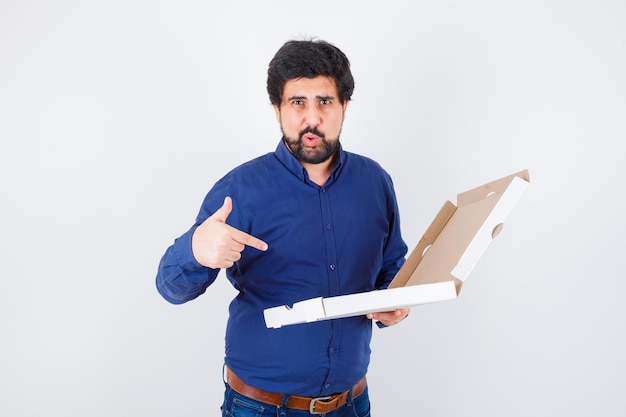 Young male pointing pizza box in shirt, jeans and looking confident. front view.