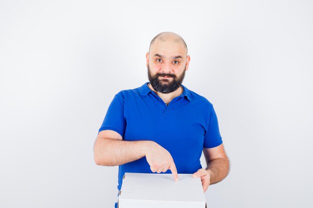 Young male pointing pizza box in t-shirt and looking joyful , front view.