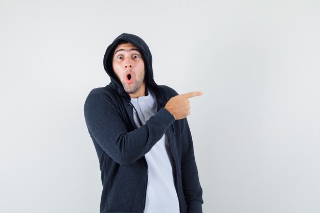 Young male pointing to the right side in t-shirt, jacket and looking wondered. front view.