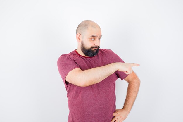 Young male pointing to the right side in t-shirt and looking wondered. front view.