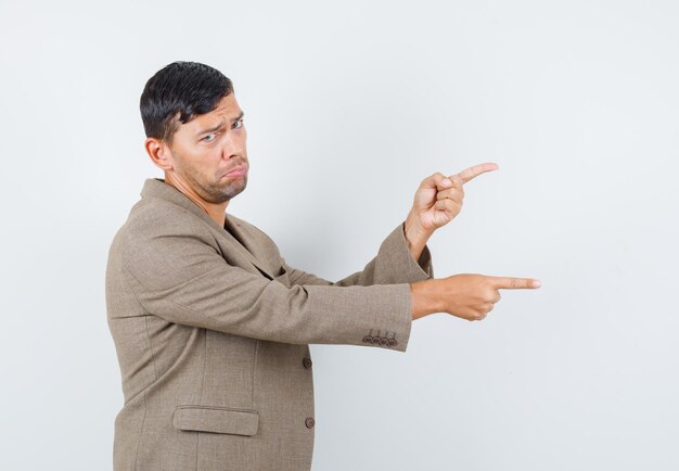 Young male pointing to the side in grayish brown jacket,black shirt and looking displeased .