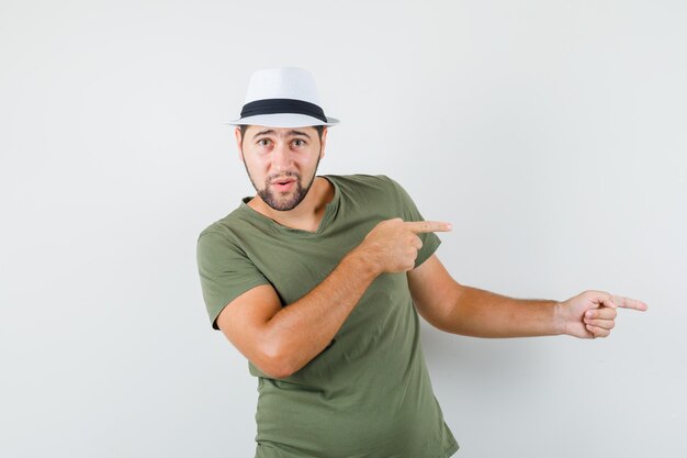 Young male pointing to the side in green t-shirt and hat and looking hesitant