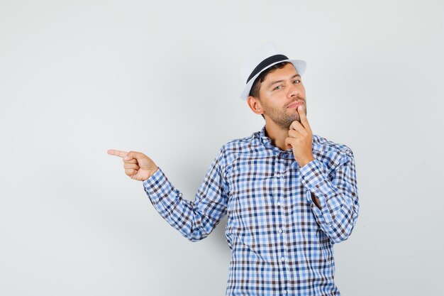 Young male pointing to the side, holding finger on chin in checked shirt