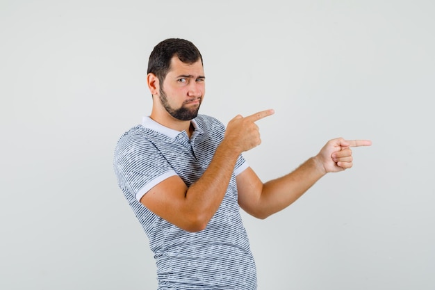 Young male pointing to the side in t-shirt and looking discontent , front view.