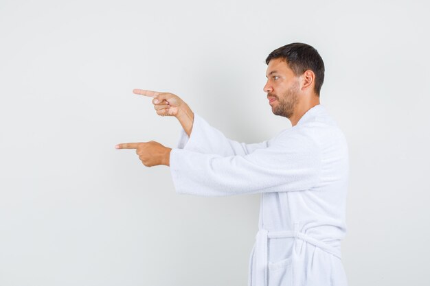 Young male pointing to side in white bathrobe and looking focused. .