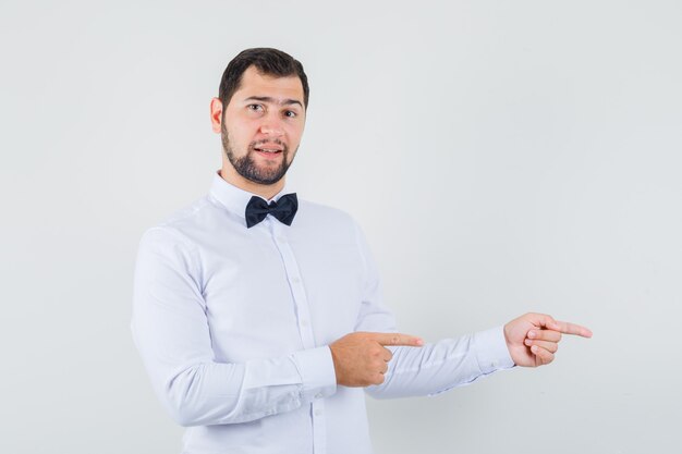 Young male pointing to the side in white shirt and looking confident. front view.