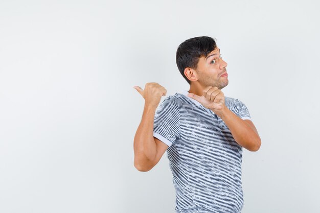 Young male pointing thumbs back in t-shirt and looking cheerful